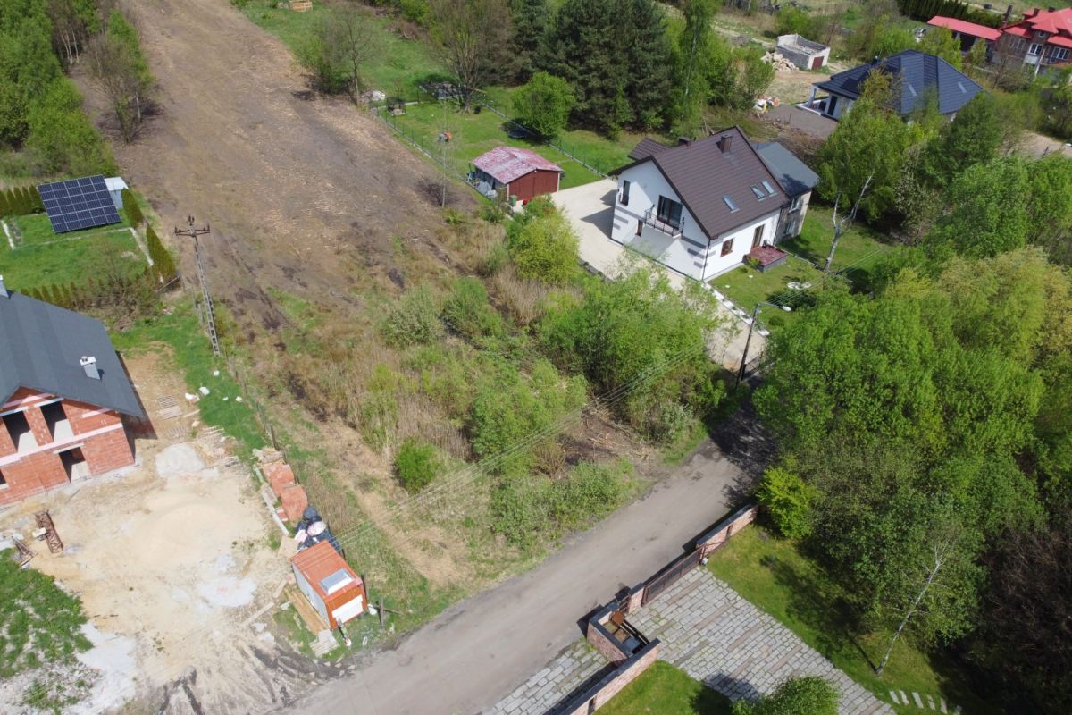 Aerial view of a suburban scene with a white two-story house, green trees, and a dirt road running beside the property.