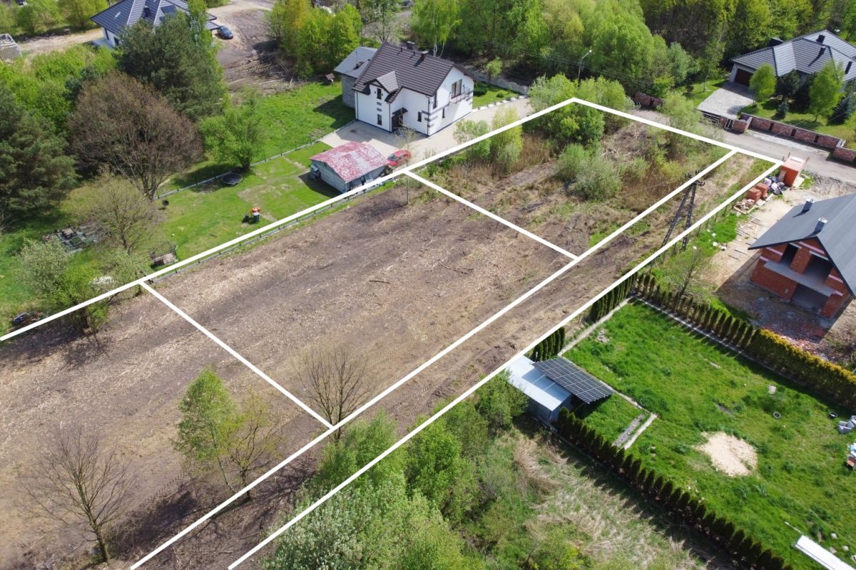 Aerial view of a residential plot divided into four outlined parcels, showing cleared and grassy lots with surrounding houses and trees.