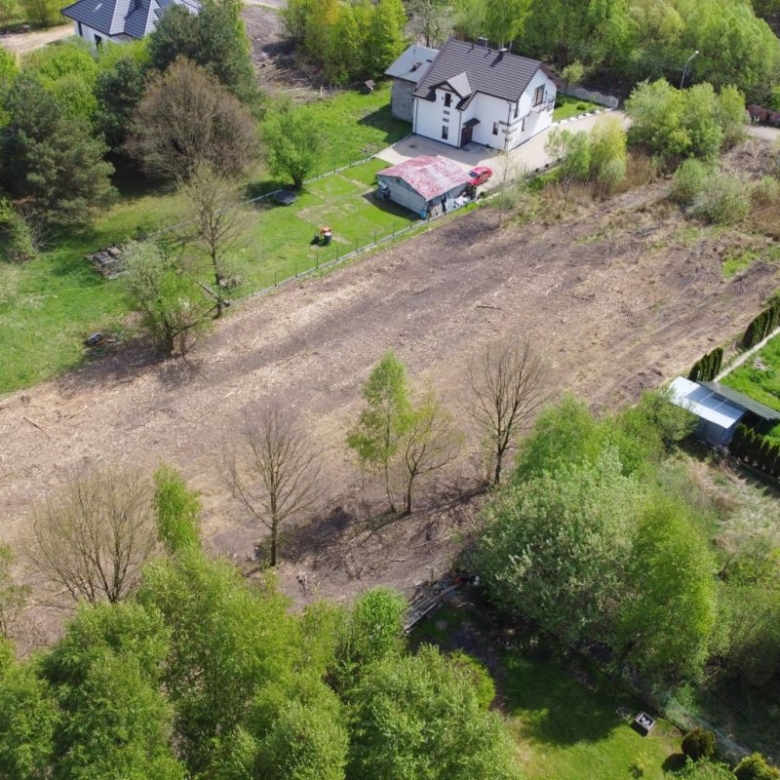 Aerial view of a partially cleared suburban lot with scattered trees, nearby houses and green lawns.