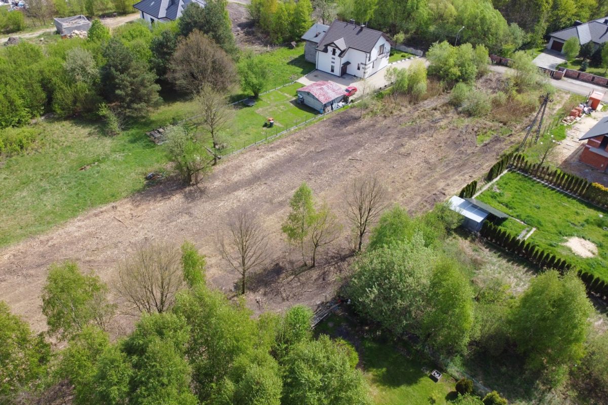 Aerial view of a partially cleared suburban lot with scattered trees, nearby houses and green lawns.