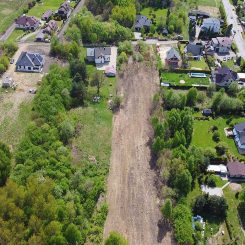 Aerial view of a suburban neighborhood with a long empty dirt lot running between houses and trees.