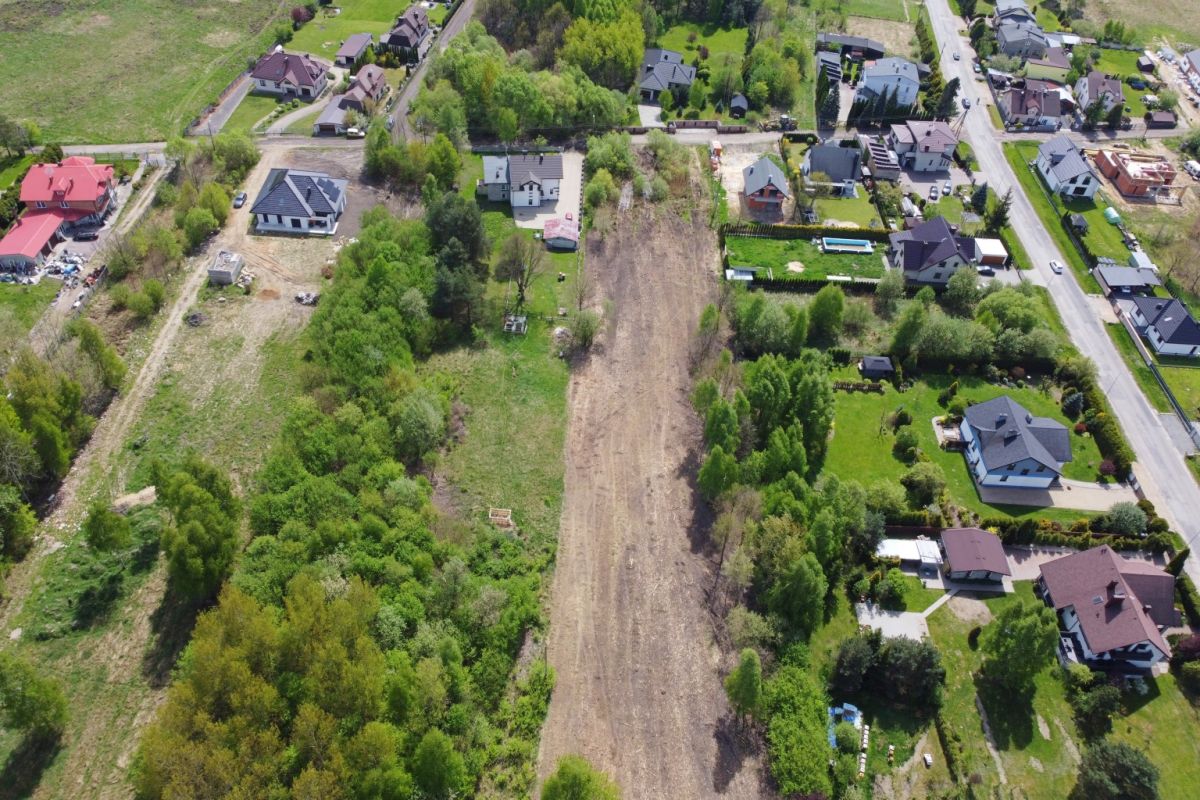 Aerial view of a suburban neighborhood with a long empty dirt lot running between houses and trees.
