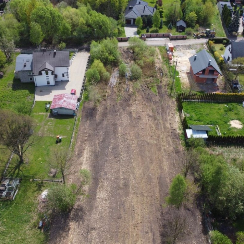 Aerial view of a vacant dirt lot between houses in a suburban neighborhood, with surrounding trees and fenced yards.