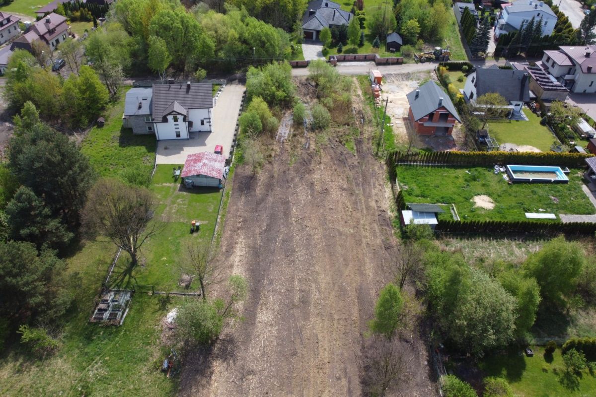 Aerial view of a vacant dirt lot between houses in a suburban neighborhood, with surrounding trees and fenced yards.