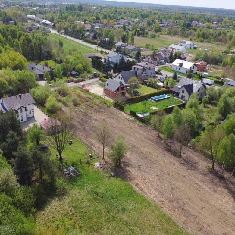 Aerial view of a suburban neighborhood with houses along tree-lined streets and a large cleared field at center-right, surrounded by greenery.
