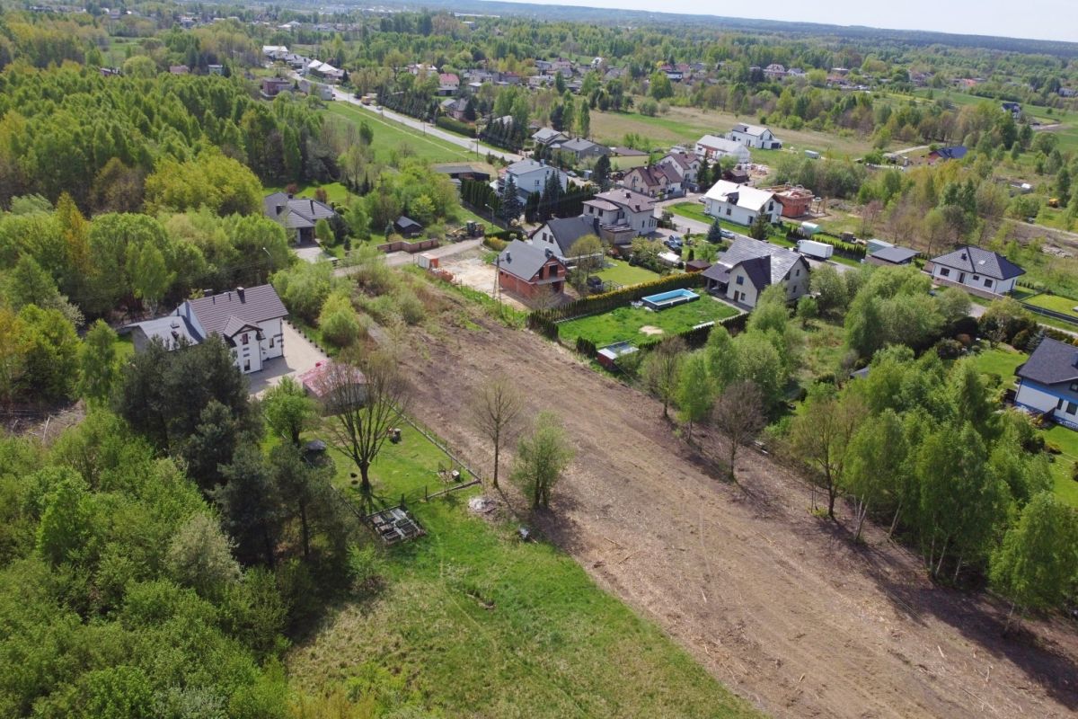 Aerial view of a suburban neighborhood with houses along tree-lined streets and a large cleared field at center-right, surrounded by greenery.