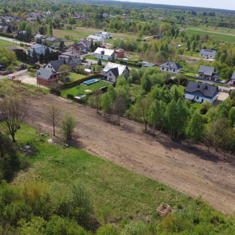 Aerial view of a suburban neighborhood with houses along tree-lined streets and a long cleared dirt path cutting through a field central to the scene.