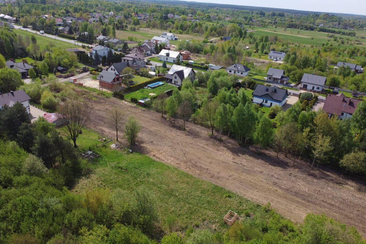 Aerial view of a suburban neighborhood with houses along tree-lined streets and a long cleared dirt path cutting through a field central to the scene.