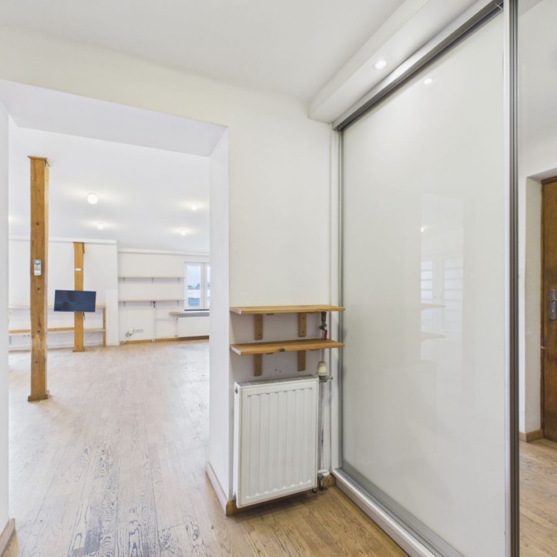Bright open-plan living area with white walls, wooden floors, exposed wooden posts, and a glass sliding door near a wooden entry door.