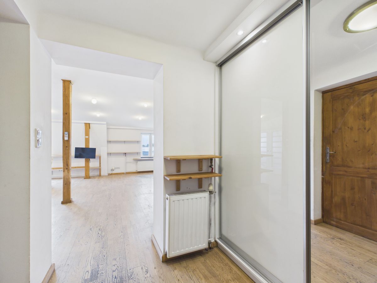 Bright open-plan living area with white walls, wooden floors, exposed wooden posts, and a glass sliding door near a wooden entry door.