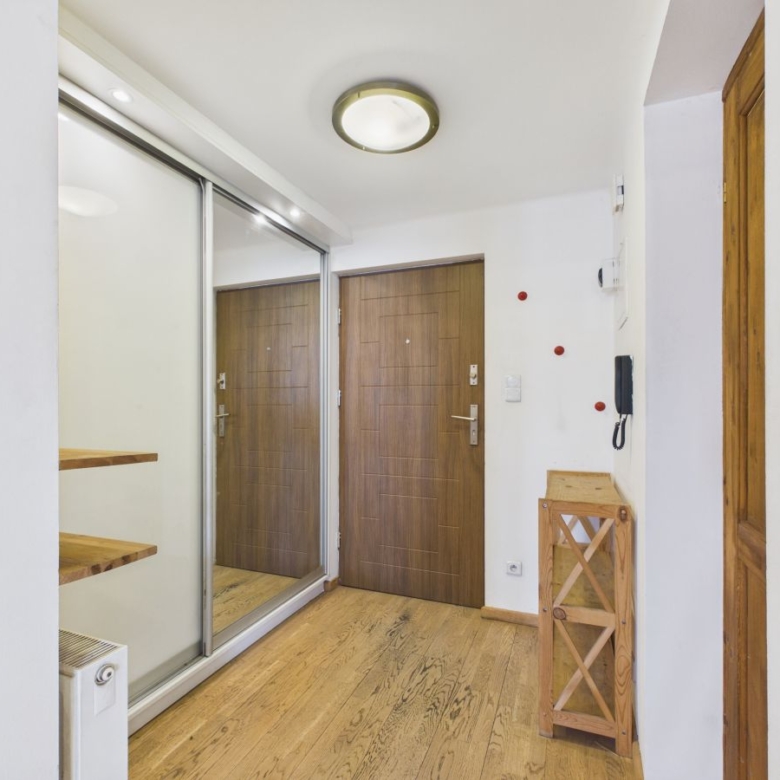 Hallway with a large mirrored sliding closet on the left, a wooden entry door ahead, and a small wooden shelf nearby on a light floor.