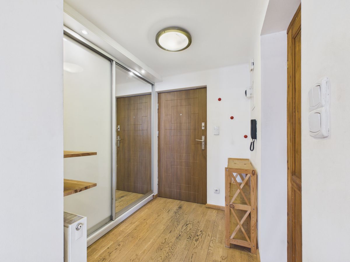 Hallway with a large mirrored sliding closet on the left, a wooden entry door ahead, and a small wooden shelf nearby on a light floor.
