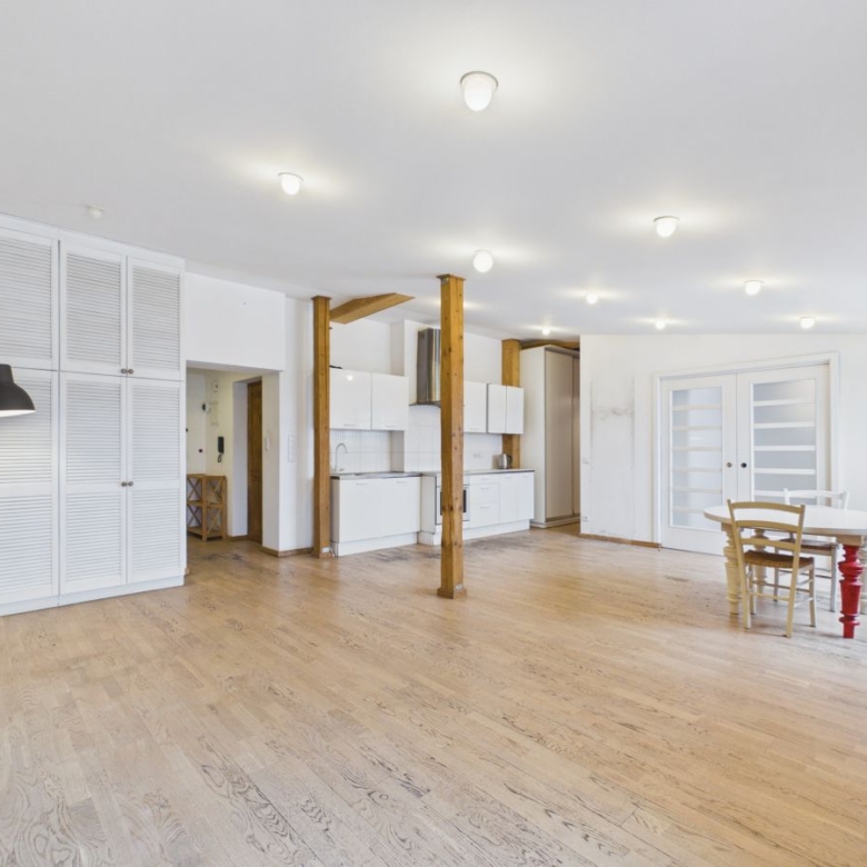 Spacious open-plan living area with white kitchen cabinets, exposed wooden posts, and light hardwood floors.