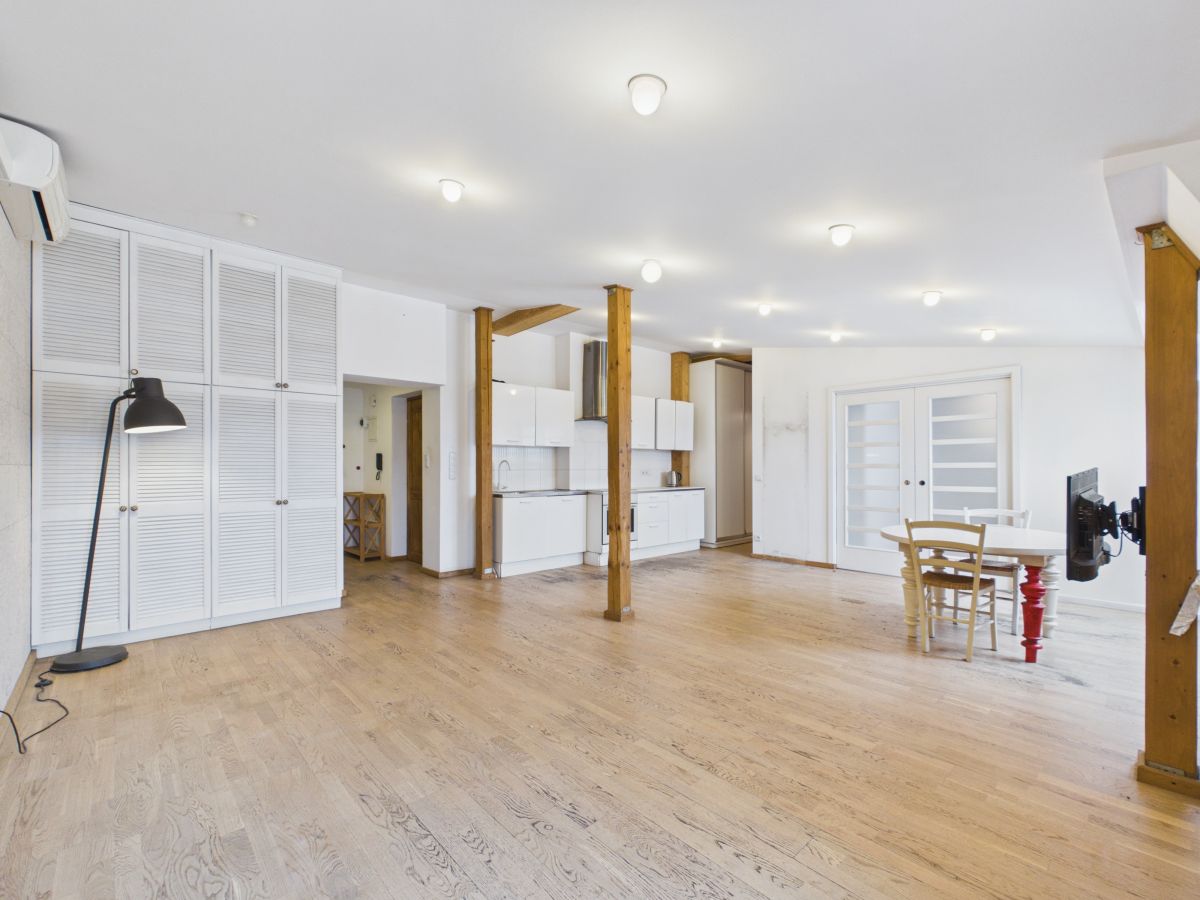 Spacious open-plan living area with white kitchen cabinets, exposed wooden posts, and light hardwood floors.