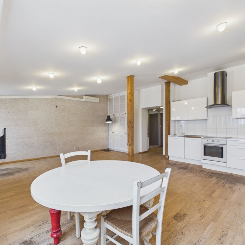 Open-plan kitchen and dining area with a round white table, white chairs, and exposed wooden beams on light wooden floors.