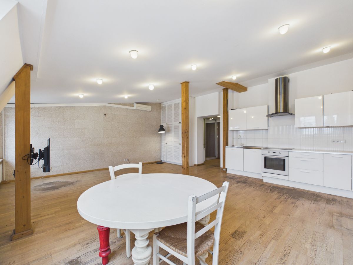 Open-plan kitchen and dining area with a round white table, white chairs, and exposed wooden beams on light wooden floors.