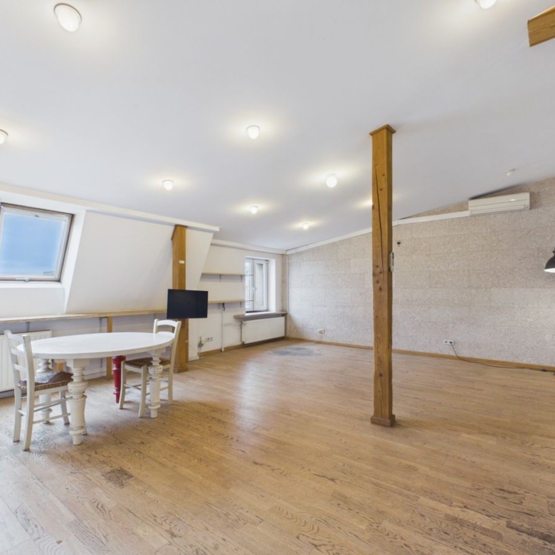 Bright loft room with skylight windows, a white round table and chairs, a wooden pillar, floor lamp, and wall-mounted TV.
