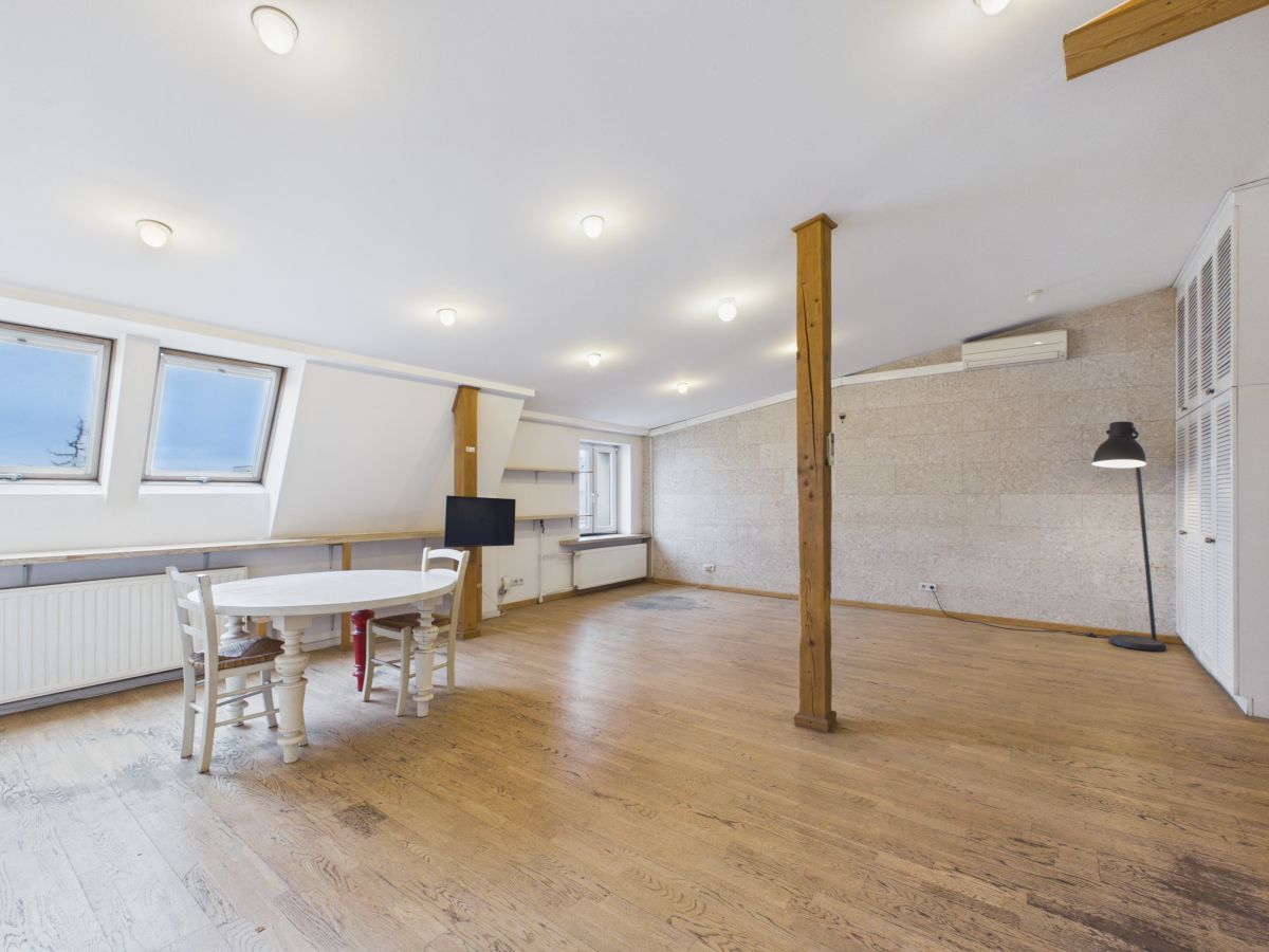 Bright loft room with skylight windows, a white round table and chairs, a wooden pillar, floor lamp, and wall-mounted TV.