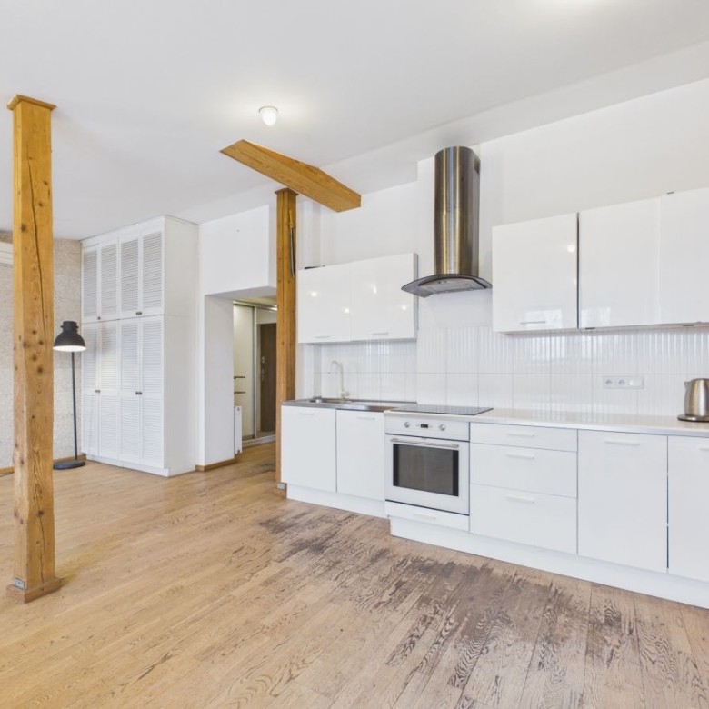 Open-plan kitchen with white cabinetry, built-in oven and stove, stainless range hood, and exposed wooden posts.