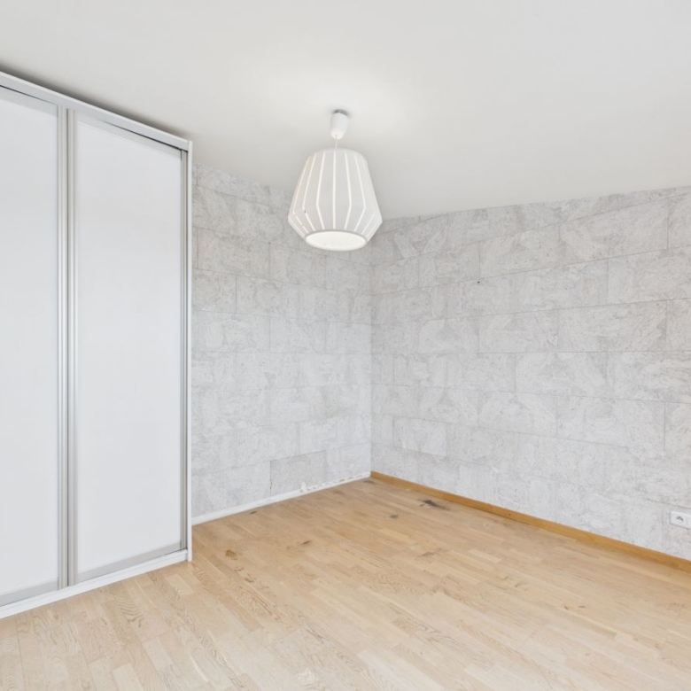 Empty room with light wood floor, white stone-tiled walls, a sliding wardrobe on the left, and a white pendant ceiling light.