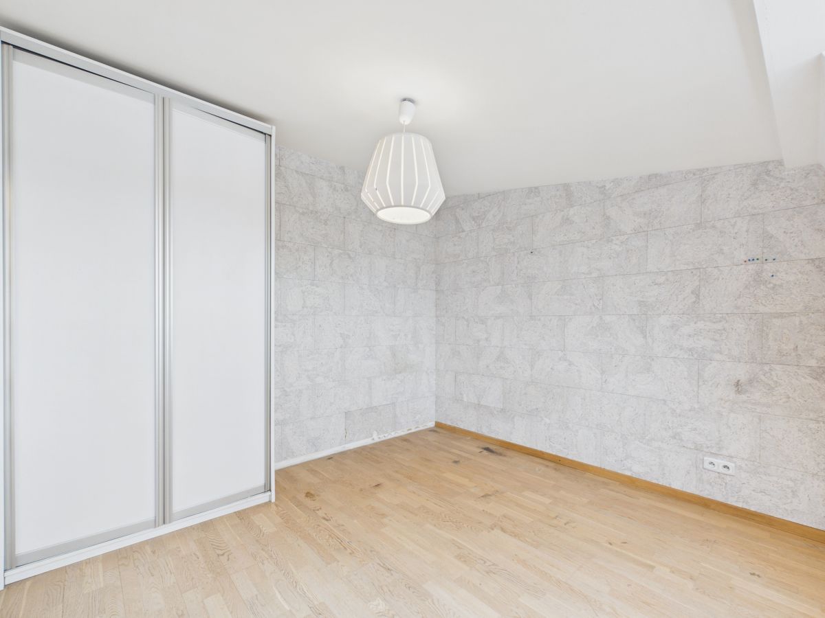 Empty room with light wood floor, white stone-tiled walls, a sliding wardrobe on the left, and a white pendant ceiling light.