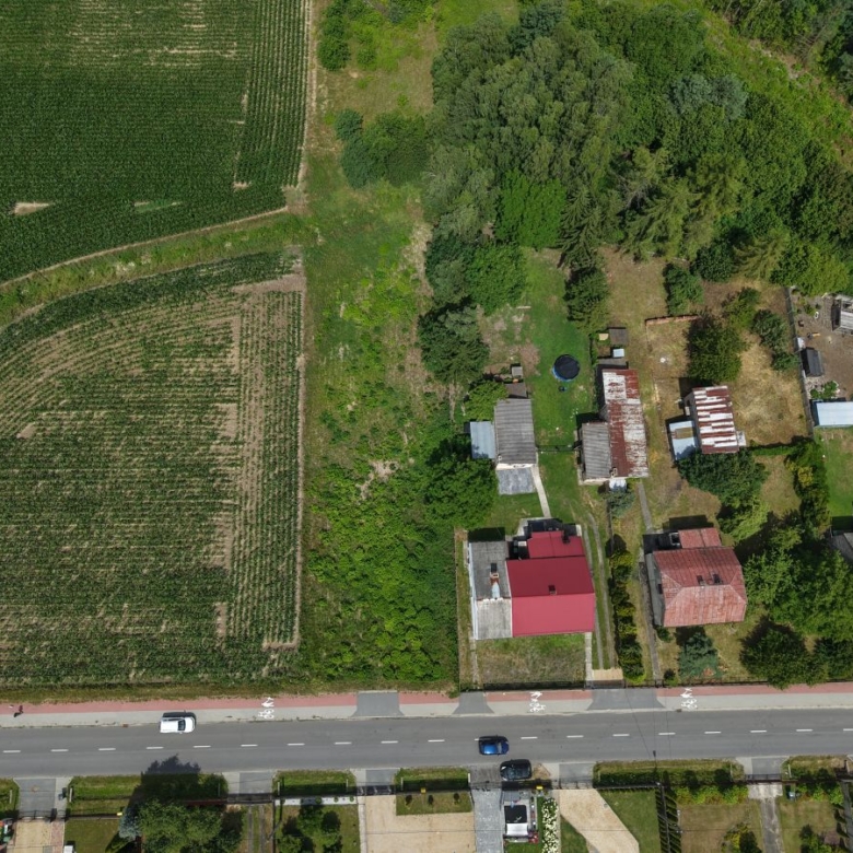 Aerial view of farmland on the left and a small cluster of houses with trees on the right, with a road at the bottom.