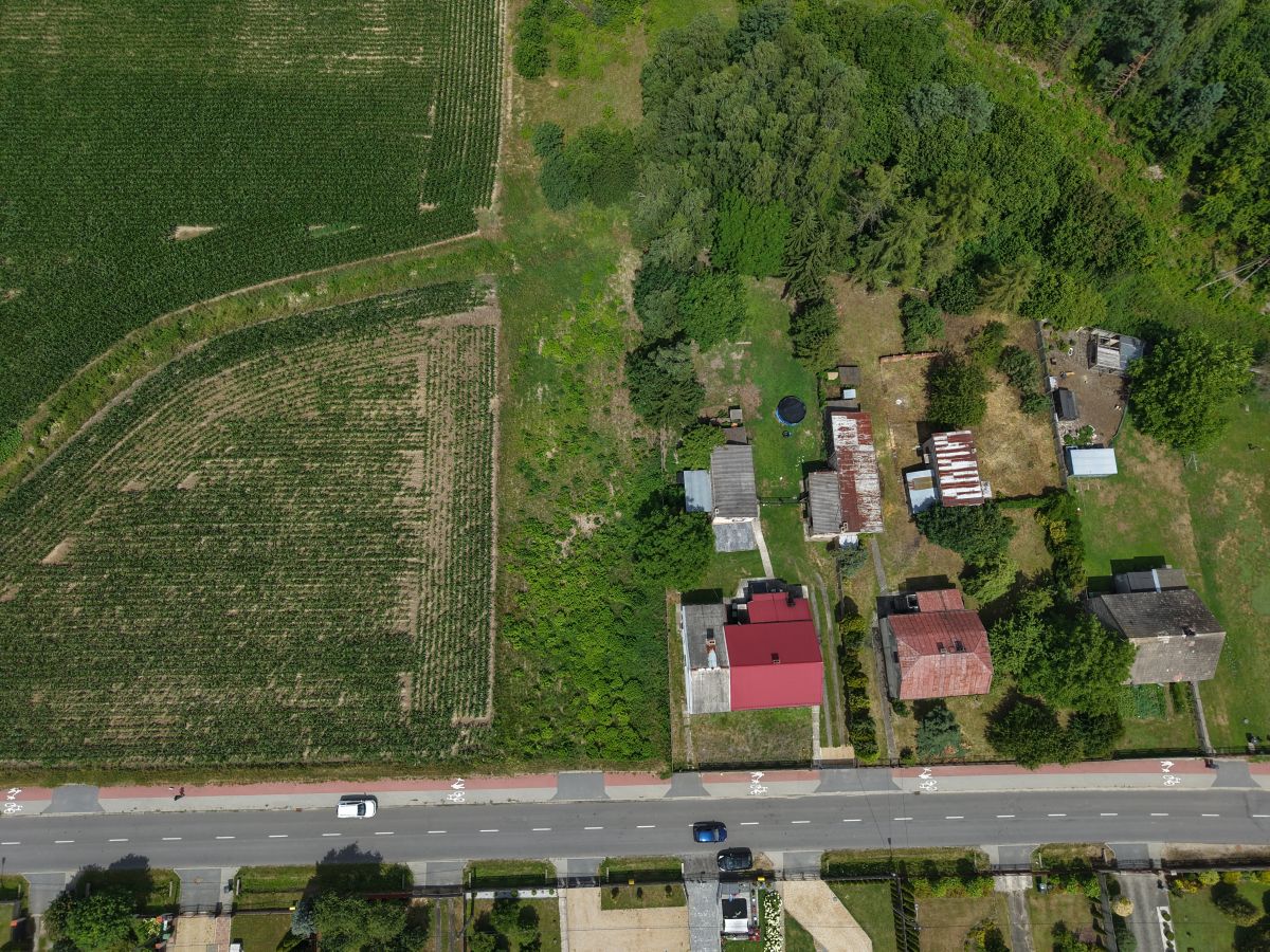 Aerial view of farmland on the left and a small cluster of houses with trees on the right, with a road at the bottom.