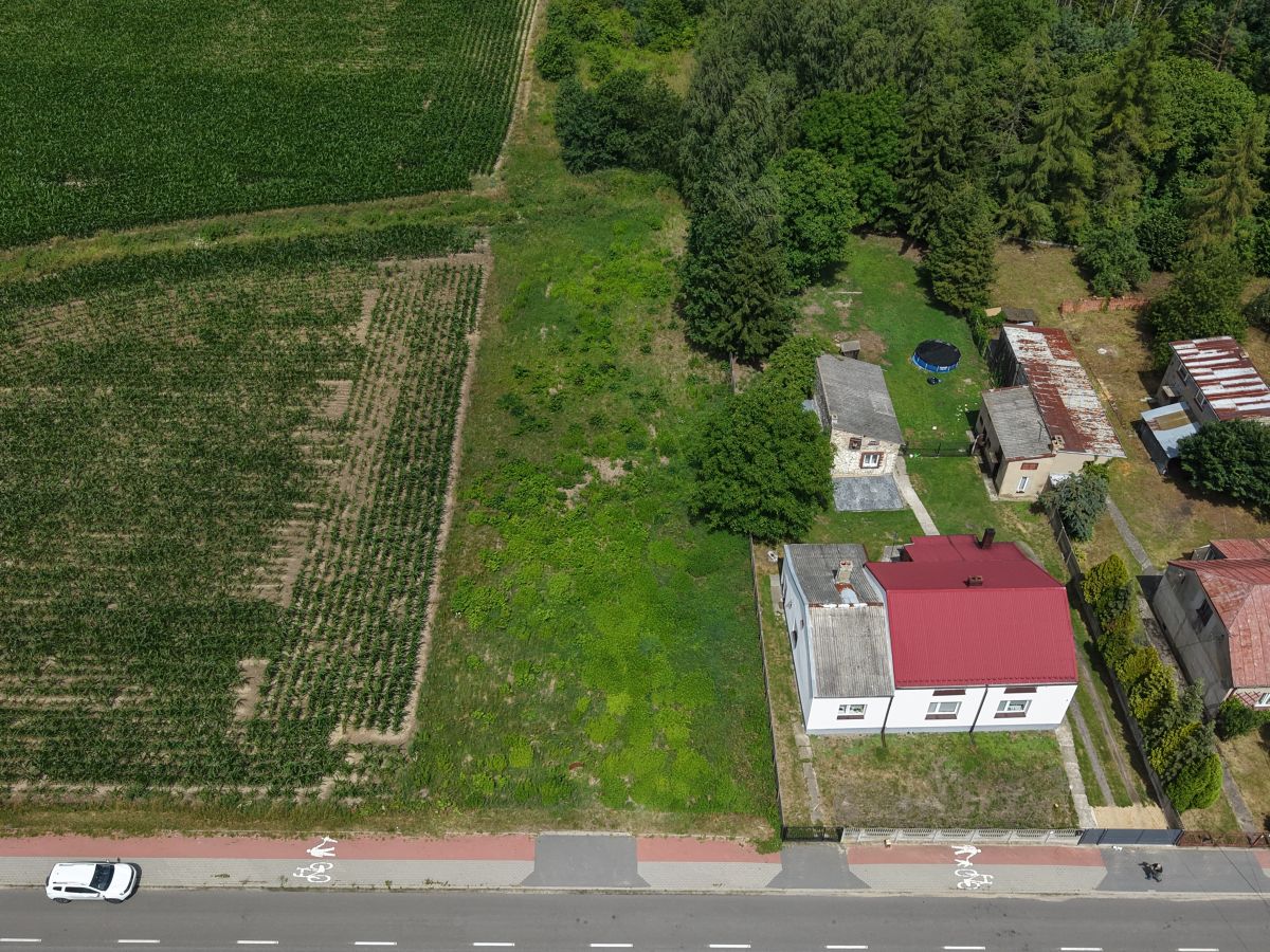 Aerial view of a rural property with a white house and red roof, several outbuildings, and a fenced yard next to green fields and trees.