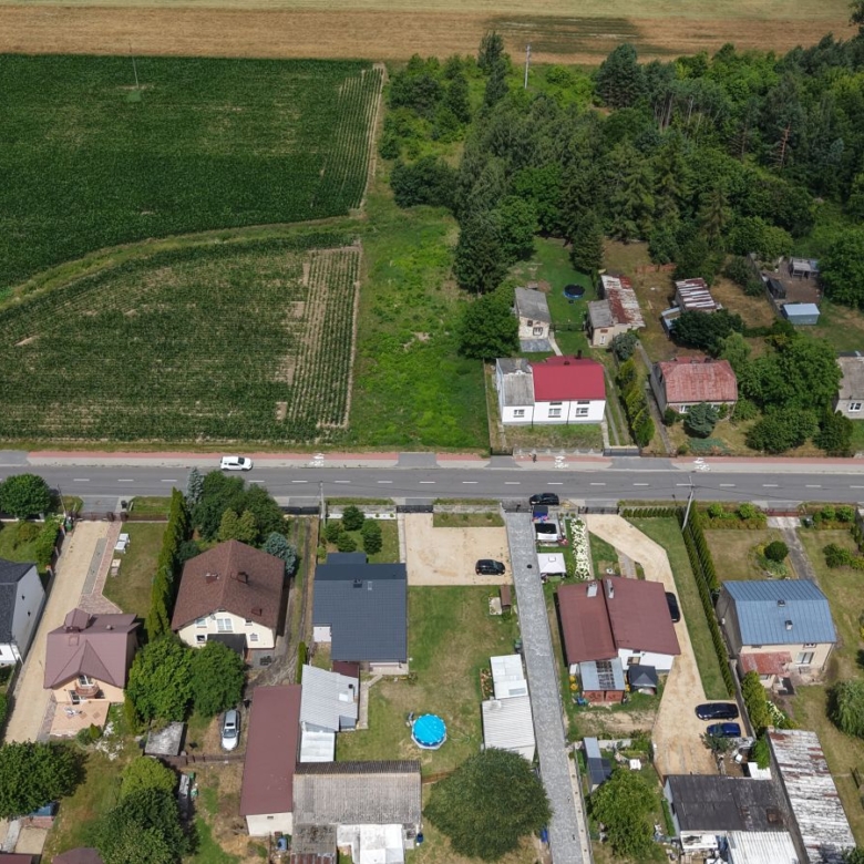 Aerial view of a residential neighborhood with houses along a road and large green fields beyond down the slope into fields and trees ahead.