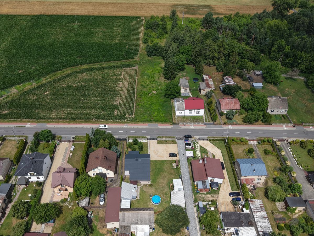 Aerial view of a residential neighborhood with houses along a road and large green fields beyond down the slope into fields and trees ahead.