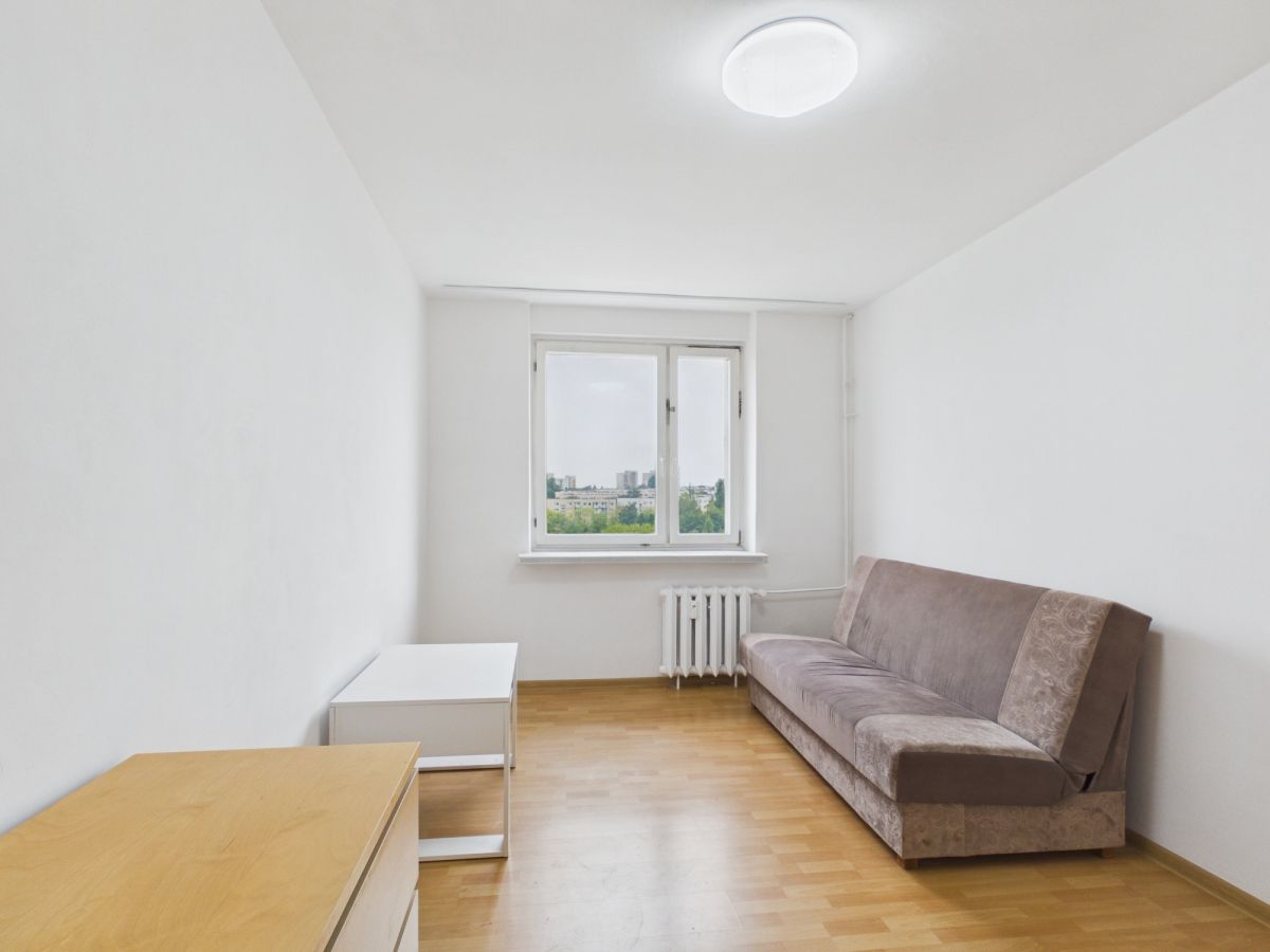 Sparse living room with a brown sofa, white walls, and a window showing a distant city view.