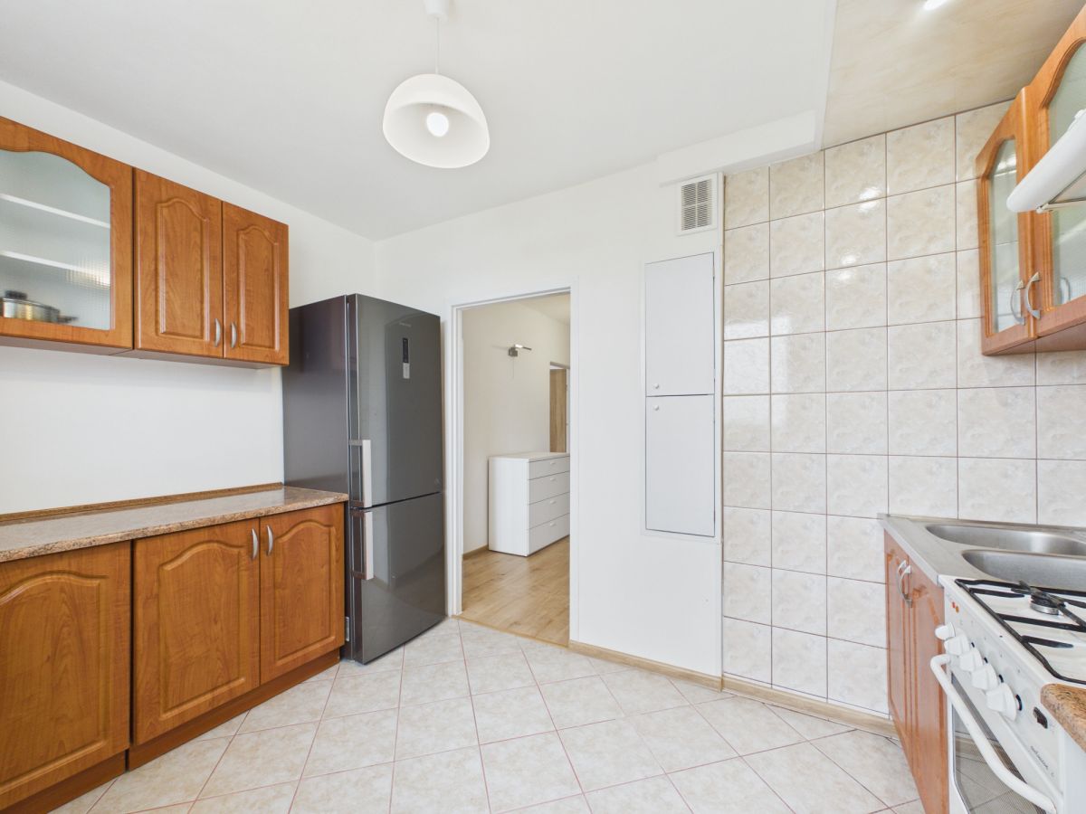 Kitchen with wooden cabinets, beige tiled walls, and a tall dark fridge near a doorway to another room.