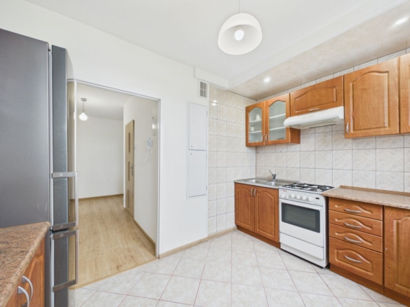 Kitchen with wooden cabinets, white stove, sink, and fridge on the left; doorway to a hallway visible to the left.