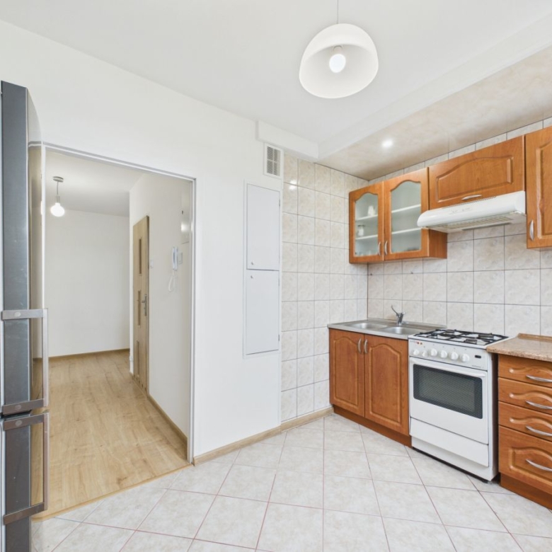 Kitchen with wooden cabinets, white stove, sink, and fridge on the left; doorway to a hallway visible to the left.