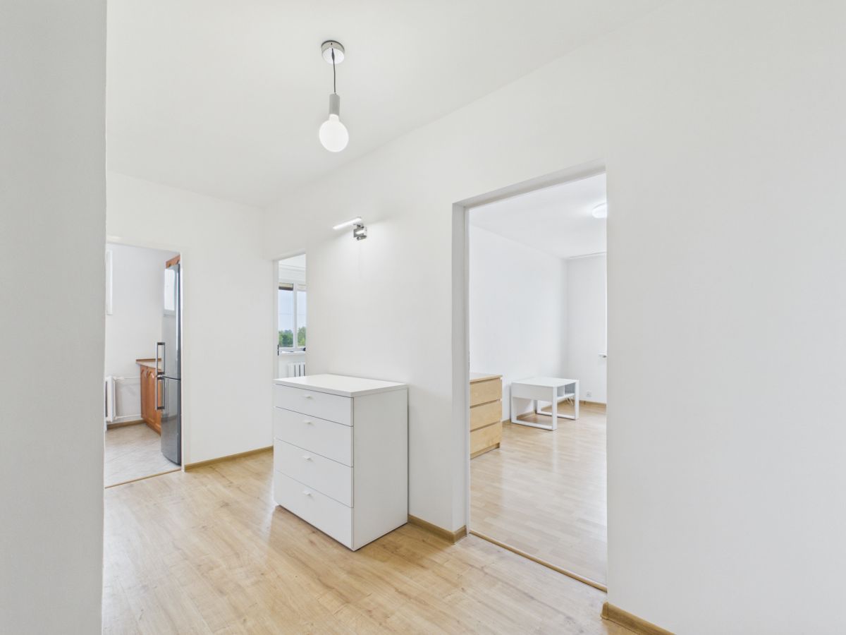 Bright, minimalist hallway with white walls, light wood floors, and a white chest of drawers near the center of the corridor.