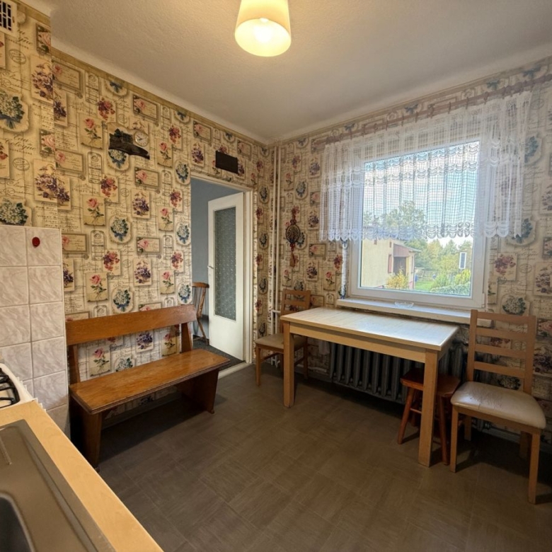 Cozy vintage kitchen with floral wallpaper, a wooden bench, and a table by a lace-curtained window.