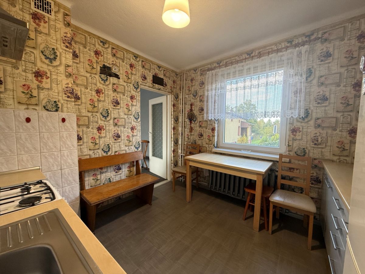 Cozy vintage kitchen with floral wallpaper, a wooden bench, and a table by a lace-curtained window.