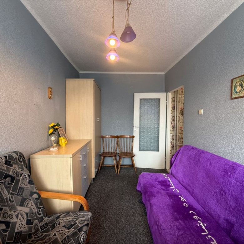 Living room with blue walls, a purple sofa bed along the right and a patterned armchair on the left, facing a wooden dresser and cabinet near the back wall.