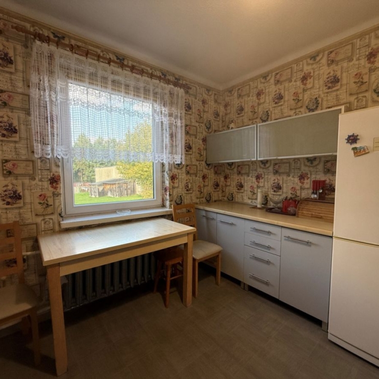 Cozy vintage kitchen with floral wallpaper, wooden table by a window and two chairs.