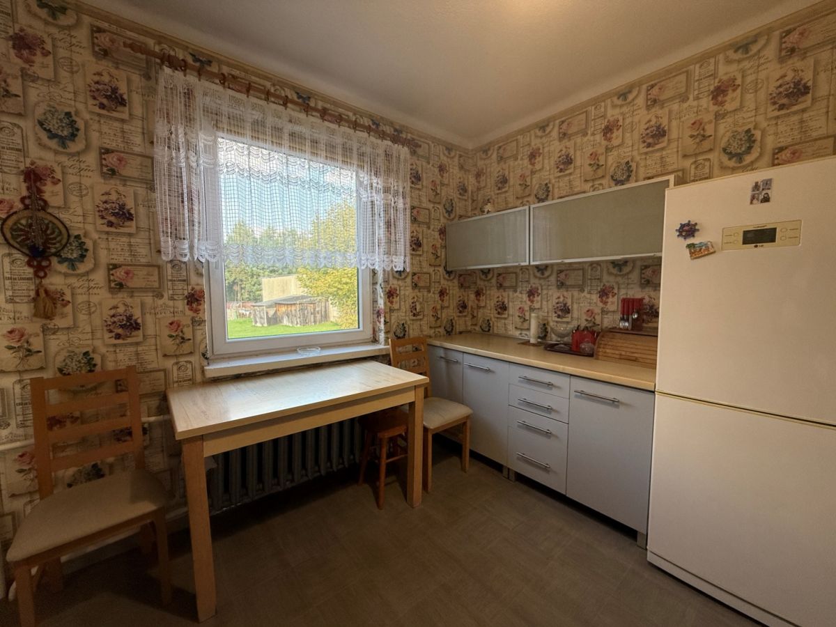 Cozy vintage kitchen with floral wallpaper, wooden table by a window and two chairs.