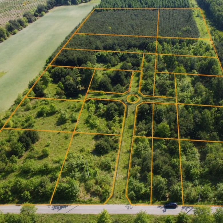 Aerial view of a wooded subdivision with orange boundary lines dividing multiple rectangular lots around a circular cul-de-sac at the center.