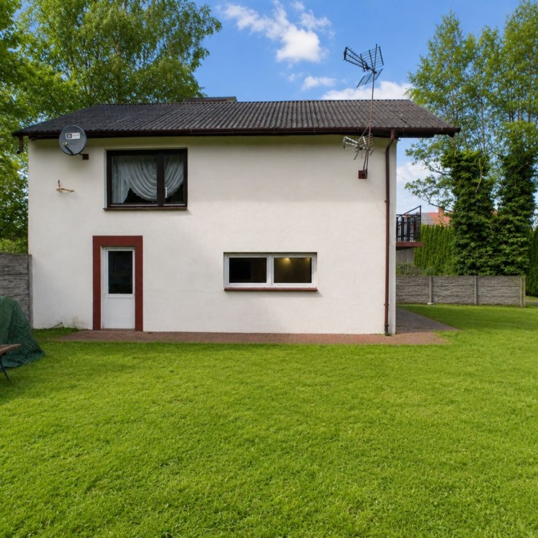 Backyard view of a small white house with a brown front door, a window above, and a grassy lawn surrounding it