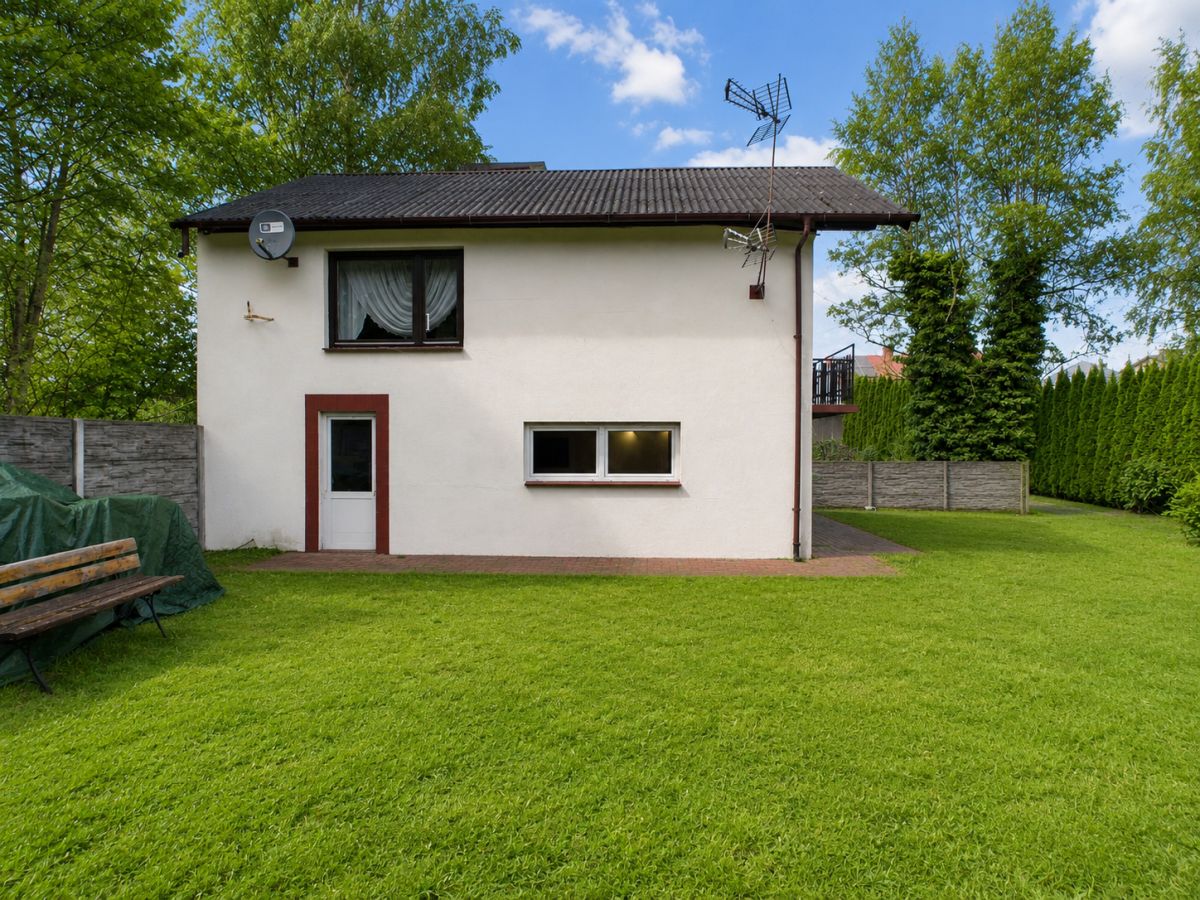 Backyard view of a small white house with a brown front door, a window above, and a grassy lawn surrounding it