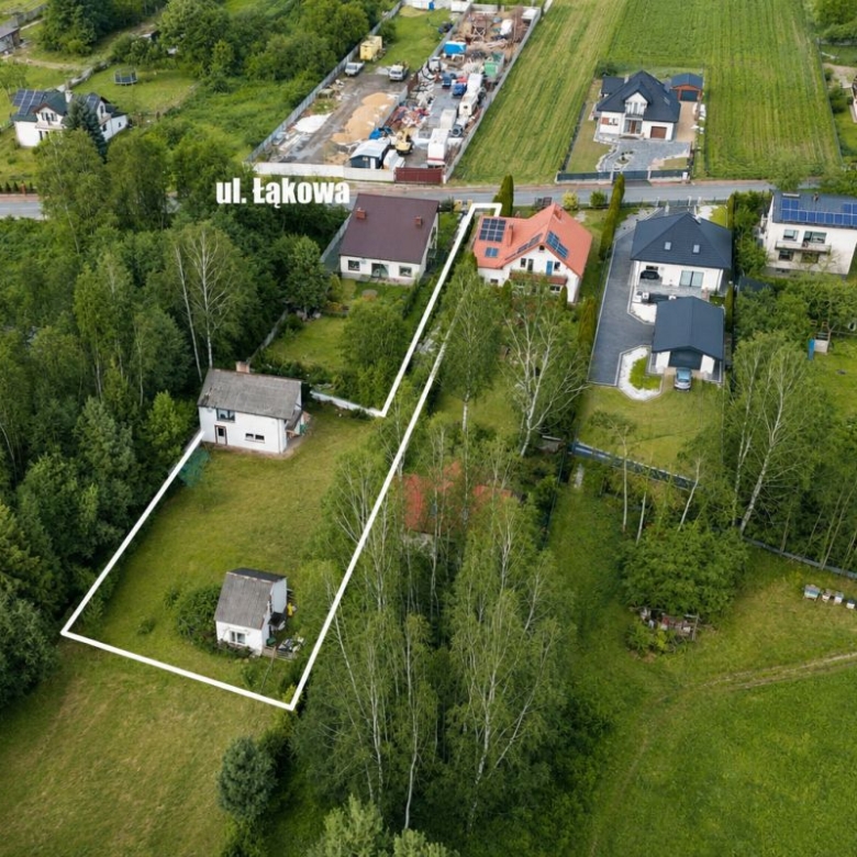 Aerial view of a residential plot outlined in white, containing two houses among trees, with surrounding homes and a street labeled ul. Łąkowa in the distance.