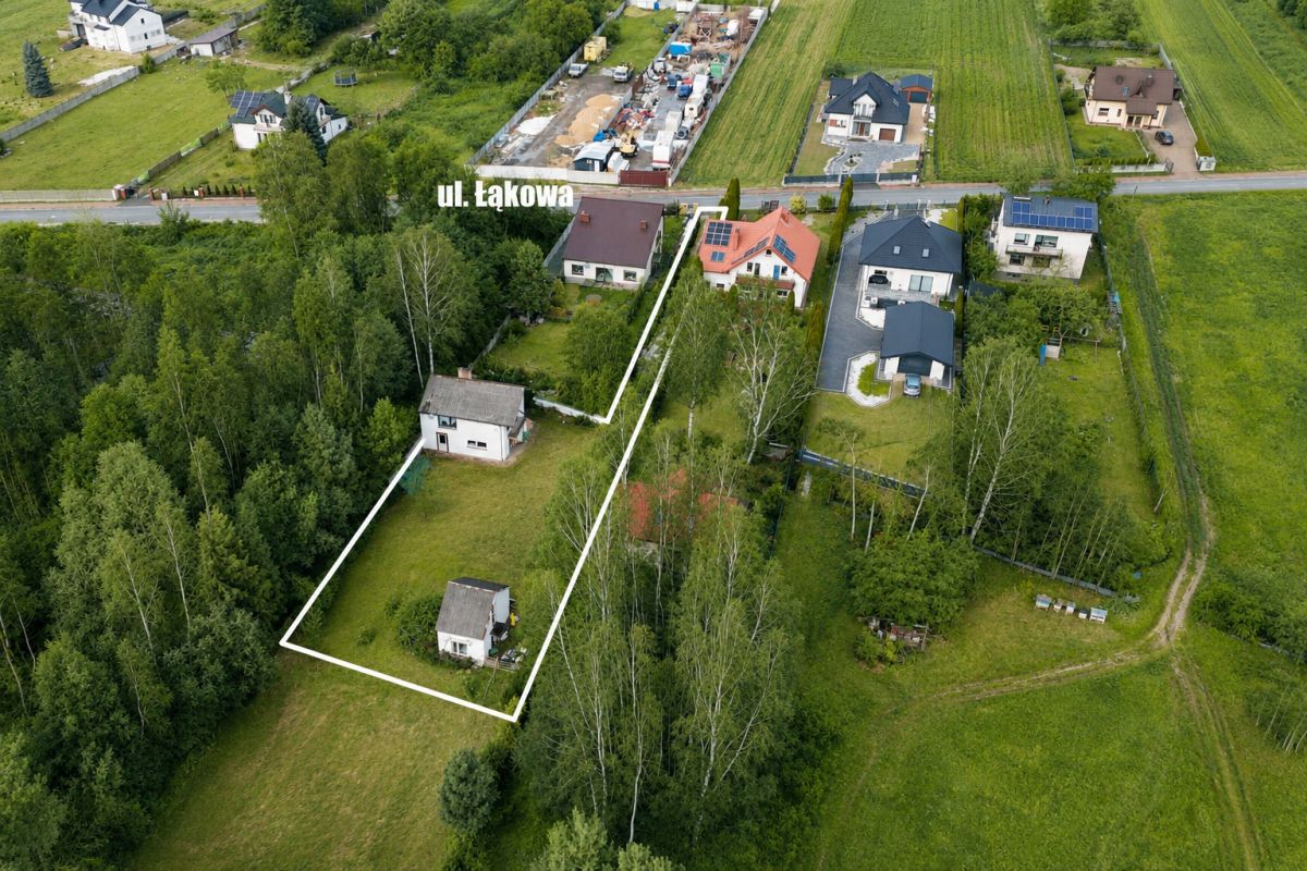 Aerial view of a residential plot outlined in white, containing two houses among trees, with surrounding homes and a street labeled ul. Łąkowa in the distance.