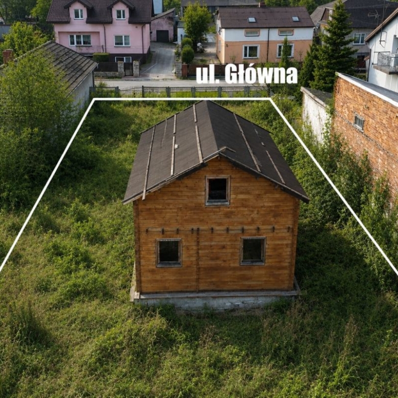 Wooden house in overgrown lot outlined as a plot, with a street label 'ul Główna' overhead in a residential area