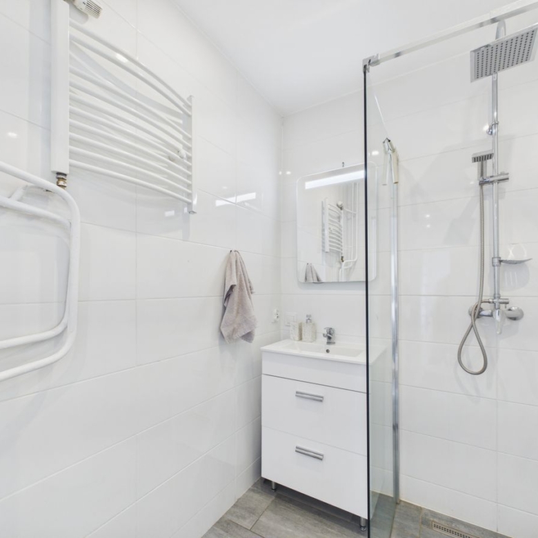 Bright white modern bathroom with a glass shower enclosure, wall-mounted vanity, and towel rail on the left wall.