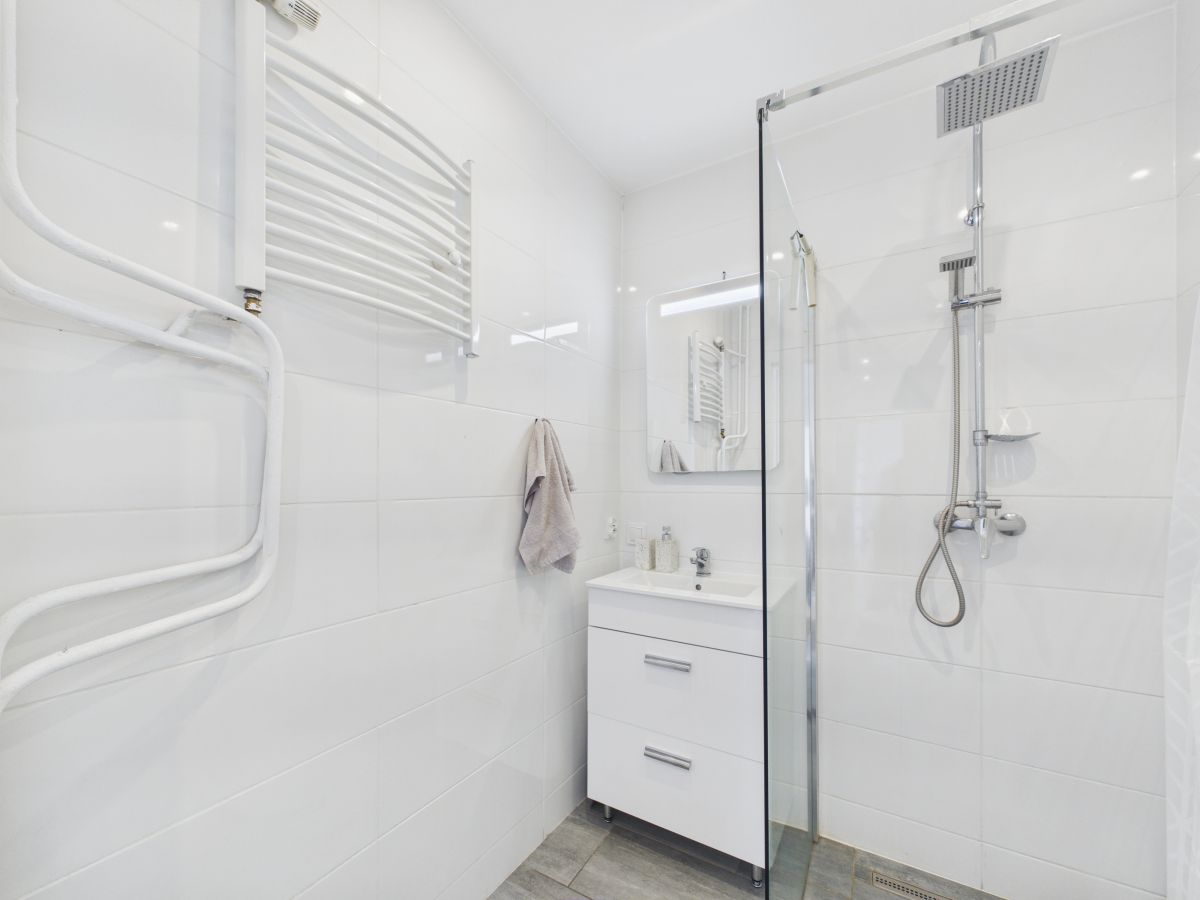 Bright white modern bathroom with a glass shower enclosure, wall-mounted vanity, and towel rail on the left wall.