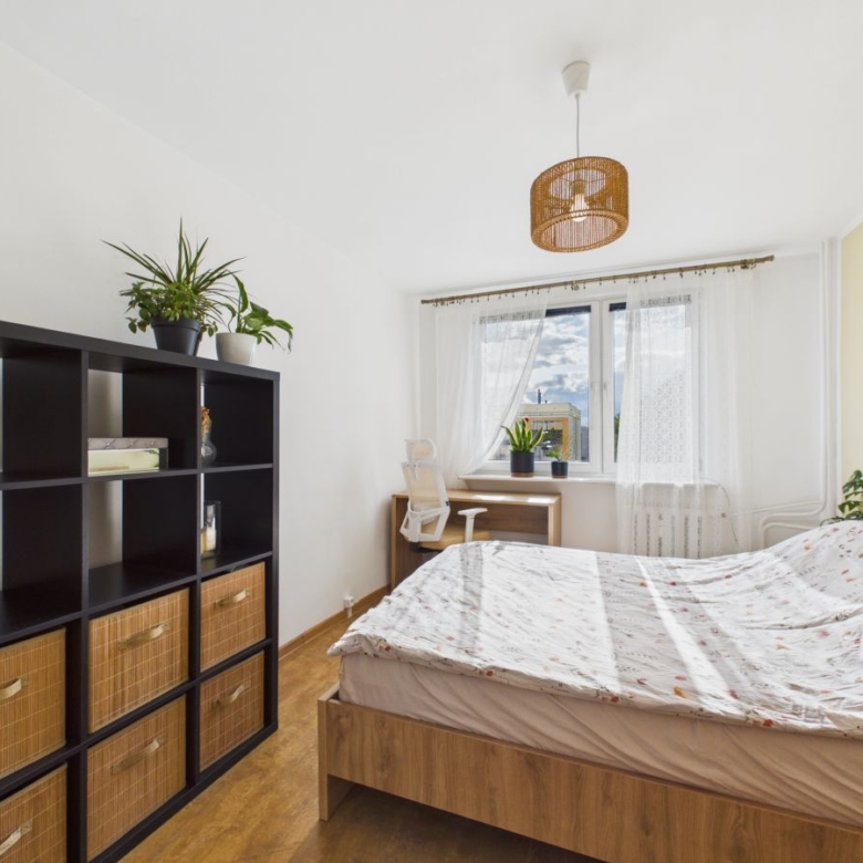 Bright bedroom with a wooden bed, floral duvet, and a black cube shelf holding wicker baskets.