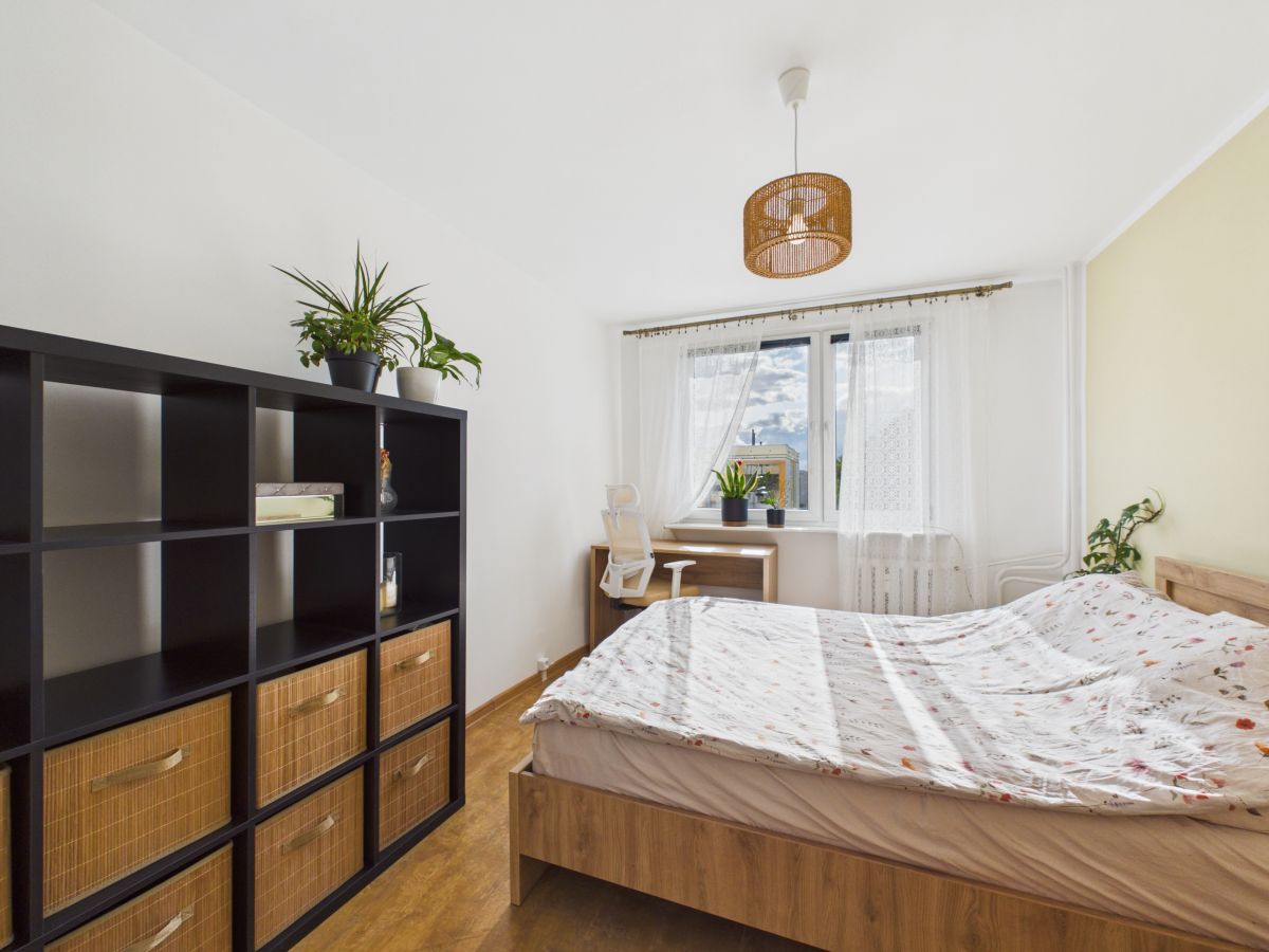 Bright bedroom with a wooden bed, floral duvet, and a black cube shelf holding wicker baskets.